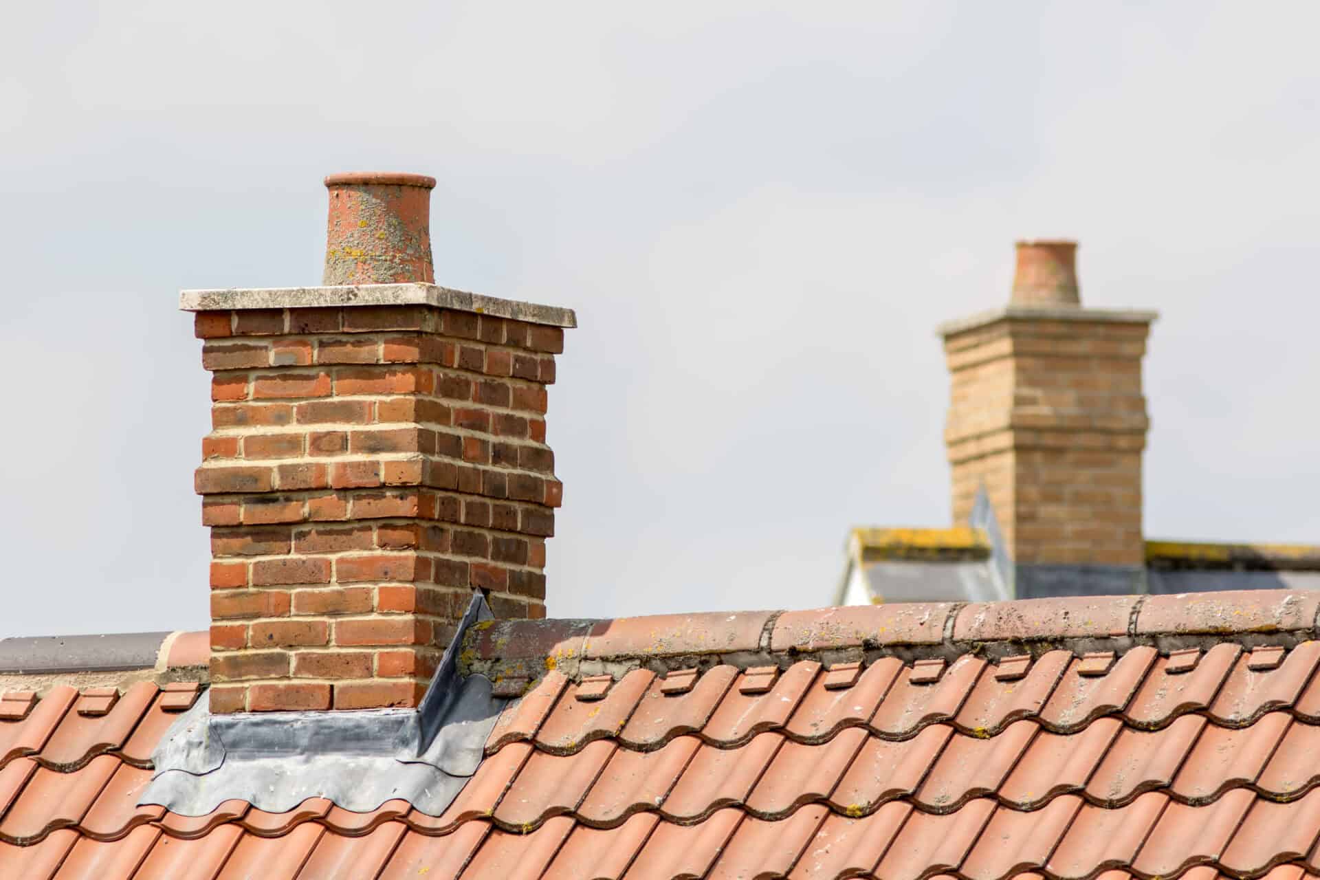 Brick chimney stack on modern contemporary house roof top. Urban housing estate tiled roof in close-up.